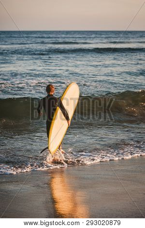 Young Boy In Black Wetsuit Carries His White And Yellow Surfboard Out To Catch Some Waves In The Pac