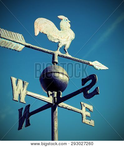Old Wind Vane With Cock On Top And Cardinal Points On The Blue Sky With Vinrtage Toned Effect