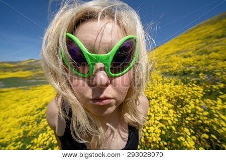 Spooky, Creepy Blonde Woman Wearing Green Alien Sunglasses In A Field Of Goldfield Wildflowers In Ca