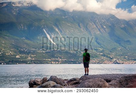 Young man standing in front of mountain and lake landscape at Garda Lake, Italy. - Travel, summer vacacion concept.