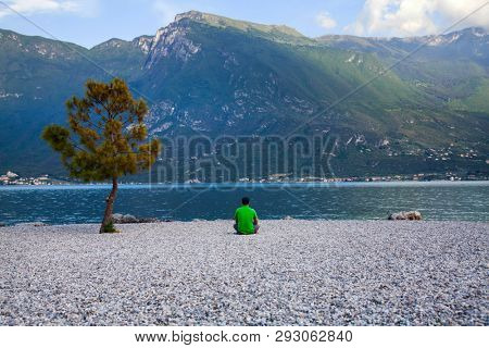 Young man sitting in front of mountain and lake landscape at Garda Lake, Italy. - Travel, summer vacacion concept.