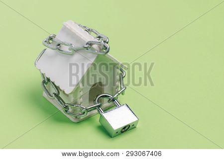Toy House Wrapped With A Chain With A Large Lock On A Green Background As A Symbol Of The Sanctity O