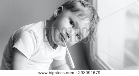 Ill Young Child With A Thermomether, Measuring The Height Of His Fever And Looking Into The Camera B
