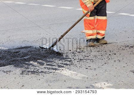 A Road Builder Collects Fresh Asphalt On Part Of The Road And Levels It For Repair In Road Construct