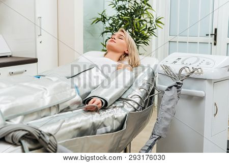 Blonde Girl Lying With Closed Eyes During Pressotherapy Session In Clinic