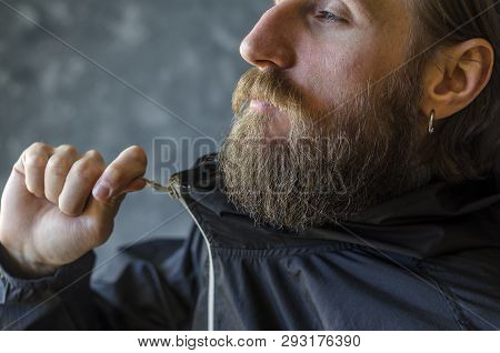 Man With A Beard Zip Up The Zipper In A Black Sports Jacket. Youth Type Of Clothing Concept