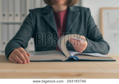 Businesswoman Reading Book At Office Desk, Searching For The Business Realted Information