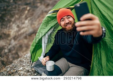 Image Of Happy Young Man Smiling, Taking Selfie In Mountains From His Smart Phone. Traveler Bearded 