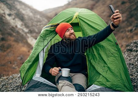 Outdoors Shot Of Happy Young Man Smiling, Taking Selfie In Mountains From His Smart Phone. Traveler 