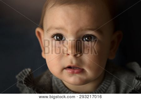Close Up Portrait Of A Surprised Baby Boy Girk Looking Up Over Dark Background