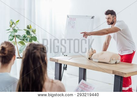 Handsome Instructor With Cpr Dummy Pointing With Finger During First Aid Training Class