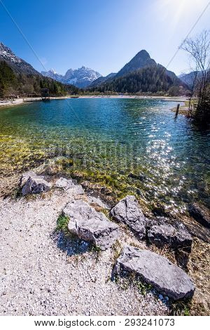 Rocks On Beach At Lake Jasna With Mountains Razor And Prisojnik On The Horizont In Slovenia