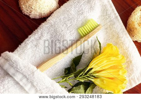 Zero-waste, Biodegradable Bamboo Toothbrush Enveloped In A White Towel With A Yellow Flower Next To 