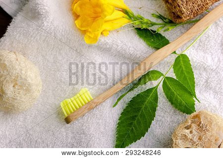 Zero-waste, Biodegradable Bamboo Toothbrush On A White Towel With A Yellow Flower Next To It.