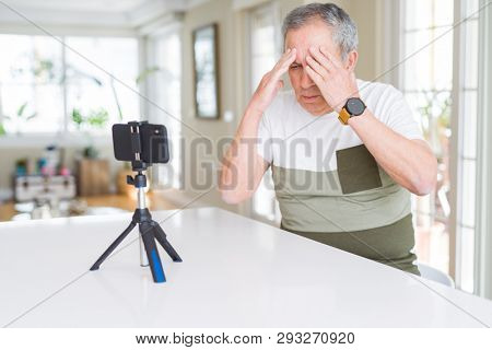 Handsome senior man doing video conference talking to the smartphone camera suffering from headache desperate and stressed because pain and migraine. Hands on head.