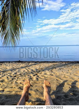 A Point Of View Shot With The Legs And Feet Of A Man Showing Lying On A Beautiful Sandy Beach Overlo