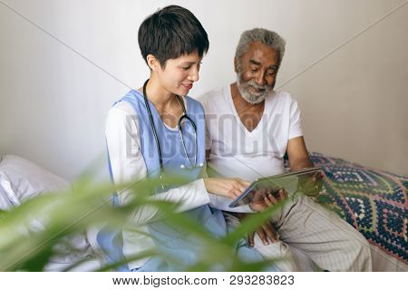 Front view of Asian female doctor and senior African-american  male patient using digital tablet at retirement home