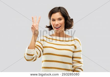 counting and people concept - happy smiling young woman in striped pullover showing three fingers over grey background