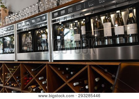 alcohol, technology and storage concept - close up of wine bottles storing in dispenser at bar or restaurant