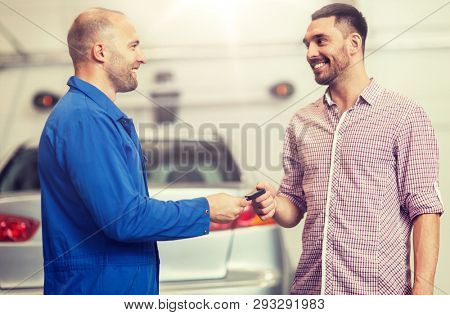auto service, repair, maintenance and people concept - mechanic with clipboard giving key to happy smiling man or owner at car shop