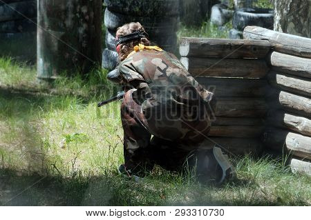 Summer. Paintball Game In The Forest. A Girl In Camouflage Clothes With A Weapon In Her Hands Is Loo