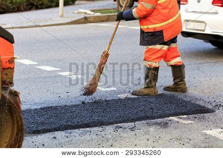 A Road Builder Collects Fresh Asphalt On Part Of The Road And Levels It For Repair In Road Construct