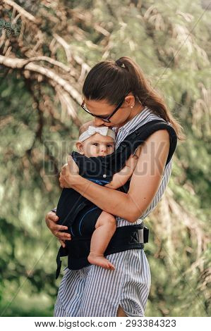Little Baby Girl And Her Mother Walking Outside Babywearing In The Ergo Carrier Concept
