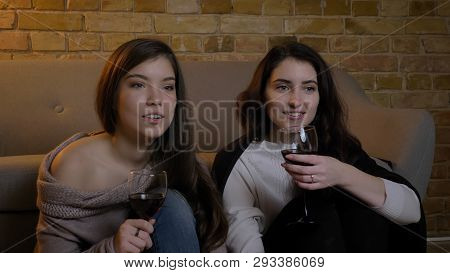 Closeup Portrait Of Two Young Pretty Women Watching Tv And Celebrating Weekend With Wine While Resti