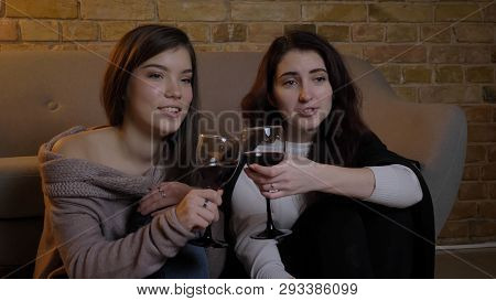 Closeup Portrait Of Two Young Pretty Women Watching Tv Chilling With Wine Celebrsting And Clinking S