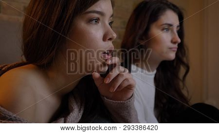 Closeup Portrait Of Two Young Pretty Women Watching Tv With Excitement In A Cozy Apartment Indoors