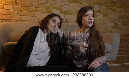 Closeup Portrait Of Two Young Pretty Women Watching A Movie Tv Chilling With Wine Sitting On The Flo