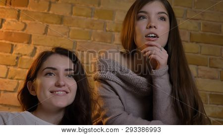 Closeup Bottom Up Portrait Of Two Young Pretty Women Watching Tv With Excitement In A Cozy Apartment