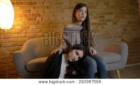Closeup Side View Portrait Of Two Young Pretty Women Watching A Movie Tv Sitting Laidback On The Flo