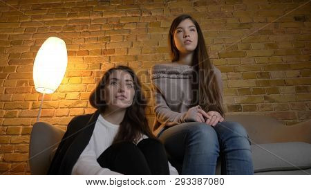 Closeup Bottom Up Portrait Of Two Young Pretty Women Watching A Movie Tv In A Cozy Apartment Indoors