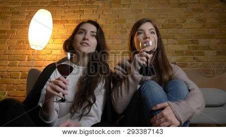 Closeup Bottom Up Portrait Of Two Young Pretty Women Watching A Tv Show Drinking Wine In A Cozy Apar