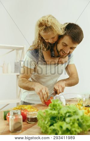 Cute Little Girl And Her Beautiful Parents Are Cutting Vegetables And Smiling While Making Salad In 