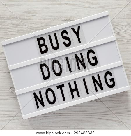 Modern Board With Words 'busy Doing Nothing' On A White Wooden Background, Top View. From Above, Fla