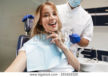 Image of a beautiful happy young woman sitting in medical dentist center take a selfie by camera.