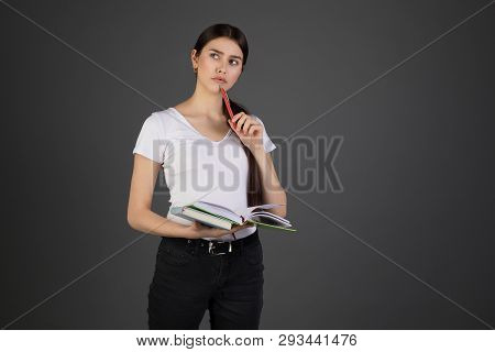 Half Length Portrait Of Thougtful Dreamy Woman Holding Red Pen In Hand Near Mouth, Books In Other Ha