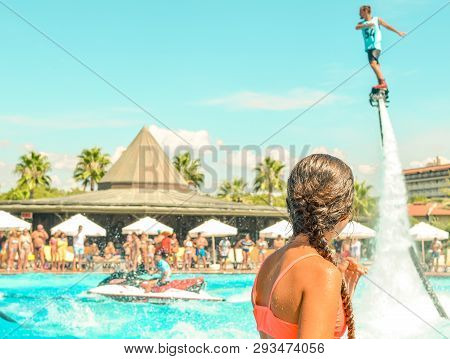 Teen Girl Watching Fly Board Watershow At The Pool. View From The Back. Summer Holidays, Fun Summert
