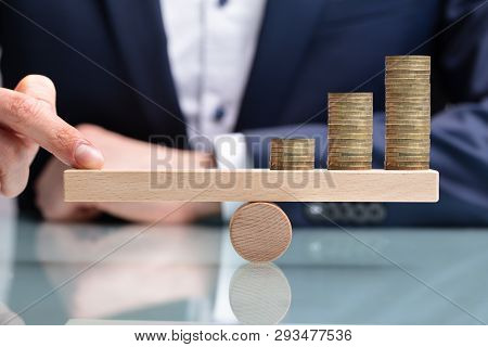 Close-up Of A Businessperson Balancing Increasing Stacked Coins With Finger On Seesaw