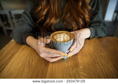 Hands Of A Young Girl Closeup, She Is Holding A Cup Of Coffee With A Beautiful Latte Art On It.