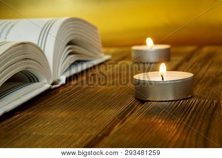 An Open Book About Religion And Faith Lies On Wooden Planks On A Golden Background. Nearby Are Lit C