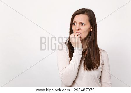 Portrait Of Preoccupied Shocked Young Woman In Light Clothes Looking Aside, Gnawing Nails Isolated O