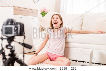 Young smiling videobloger teen girl is pointing at camera in living room