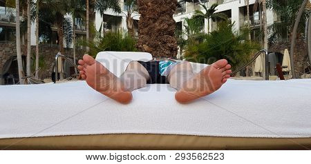 Close Up Of A Man Lays Barefoot On Soft Bed In Exotic Garden Outside A Hotel In Summer Season