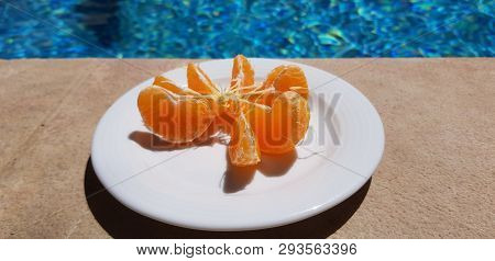 Small White Plate With Peeled Mandarin Slices Stand Near Blue Outdoor Pool