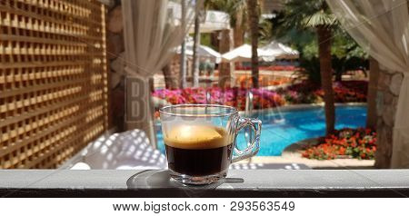 Cup With Black Coffee Standing On Hotel Window With View On Outside Pool Surrounded With Palm Trees 