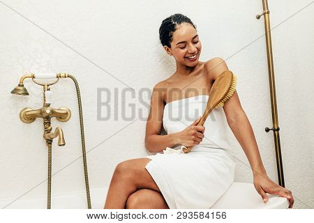 Smiling Woman Wrapped In White Towel Sitting On Bath And Dry Brushing Her Arm