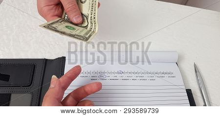 Man Gives One Dollar Bill To A Woman Holding Hand Over Notebook With Pen Marked Dates